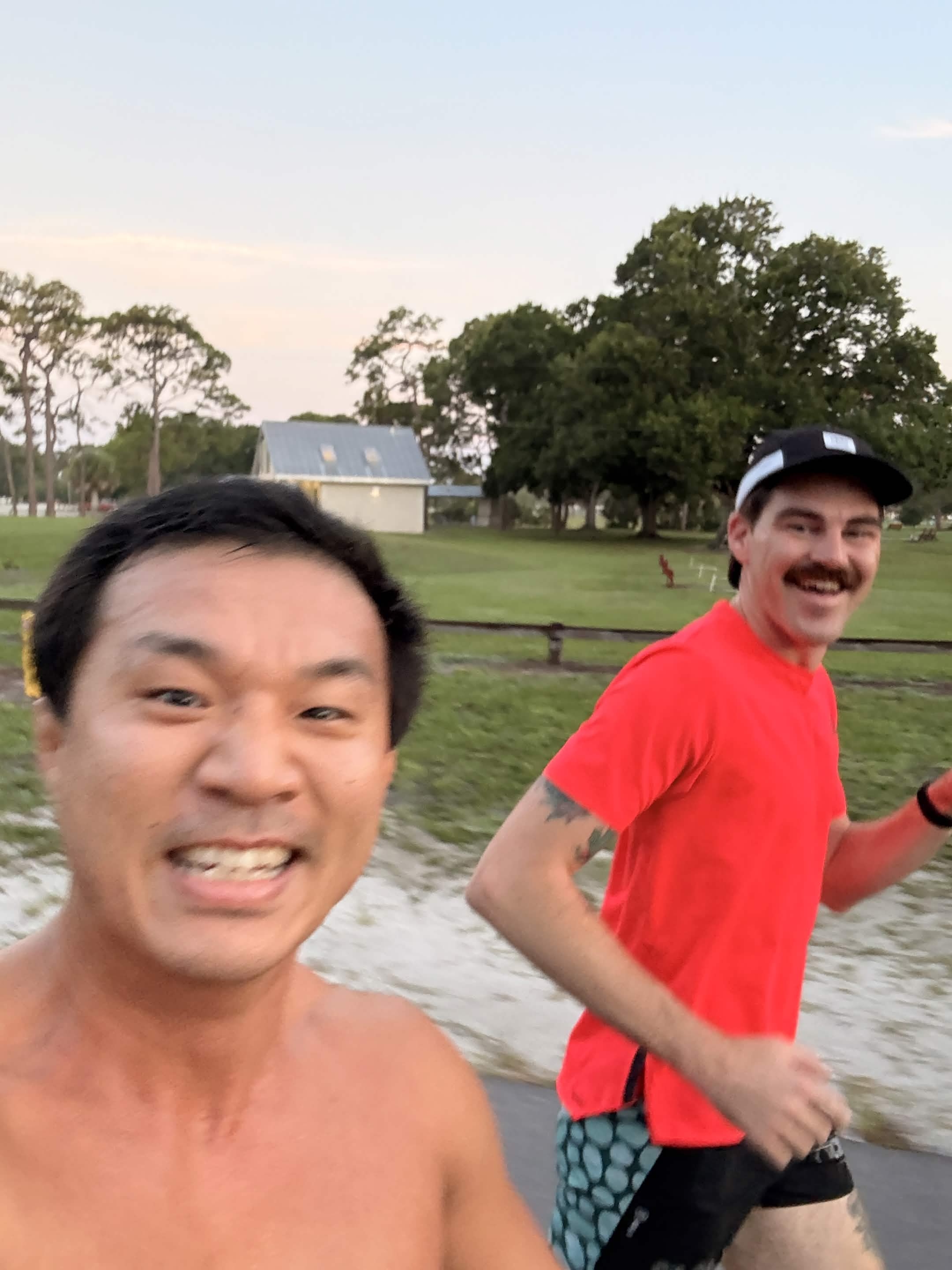 Jae and John mid-run, smiling, running past a farm in early morning light.