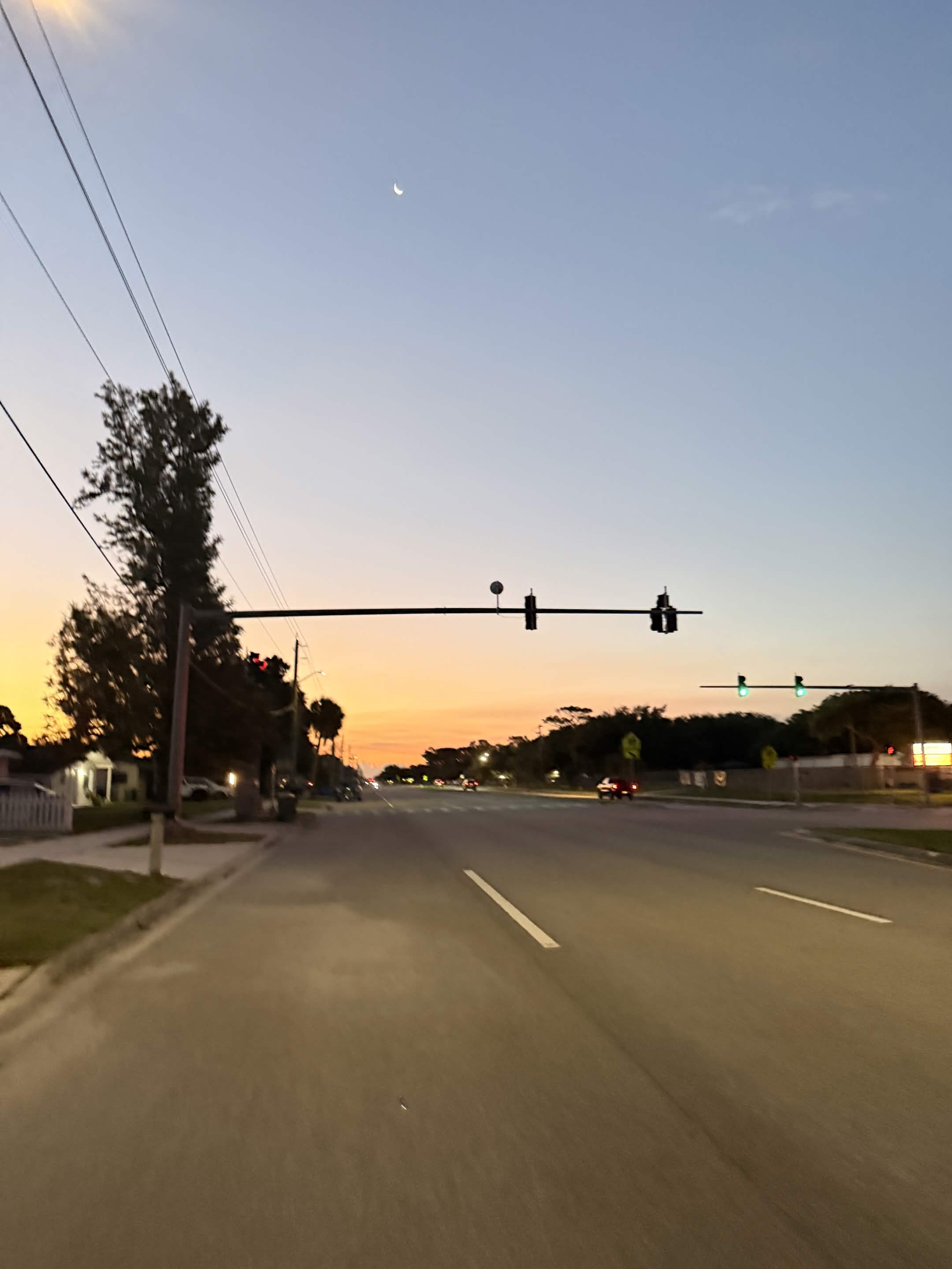 Pre-dawn Florida street with orange sky, crescent moon, and empty road.