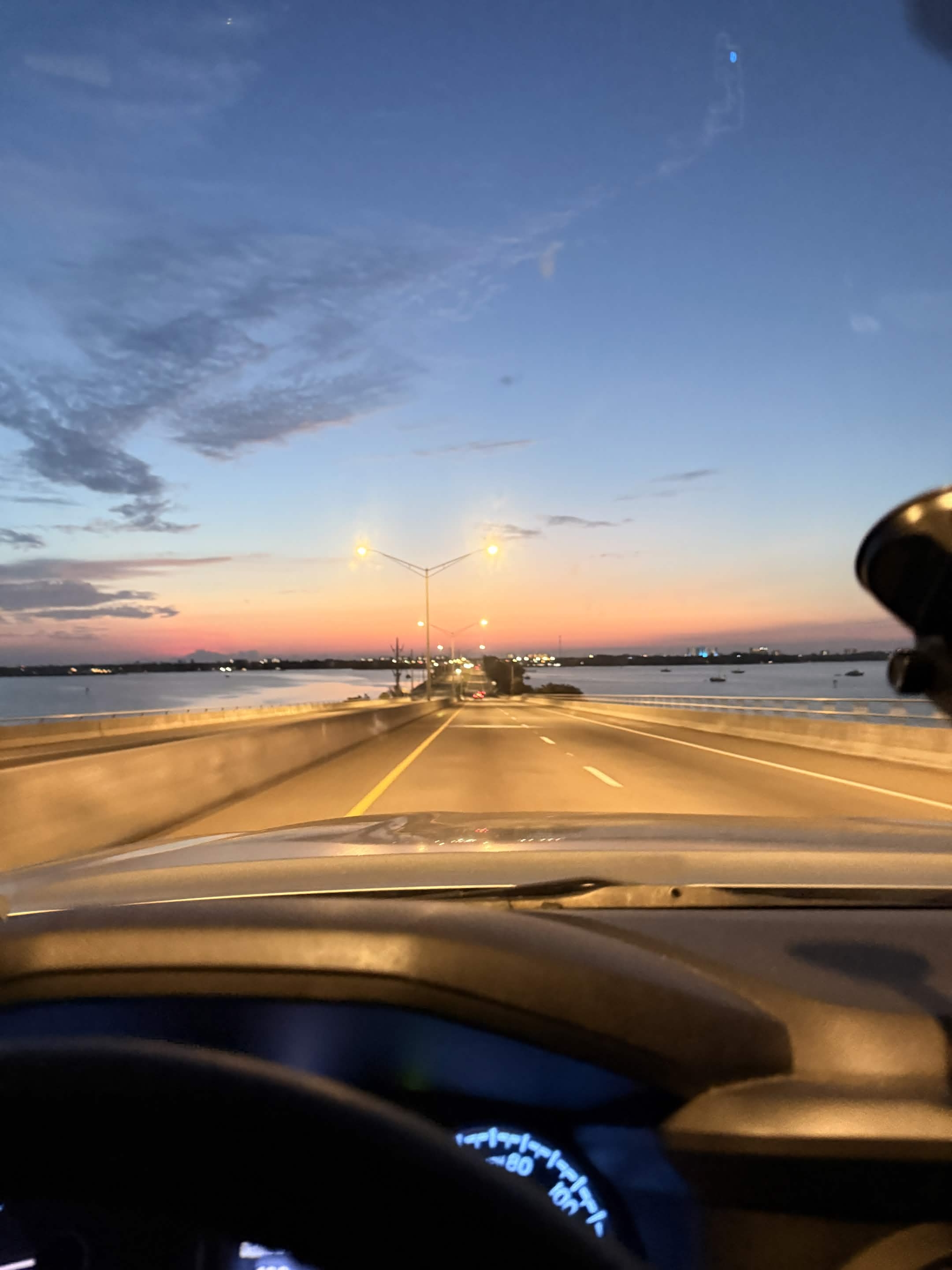 Bridge over open water at sunrise, orange sky ahead from the windshield.