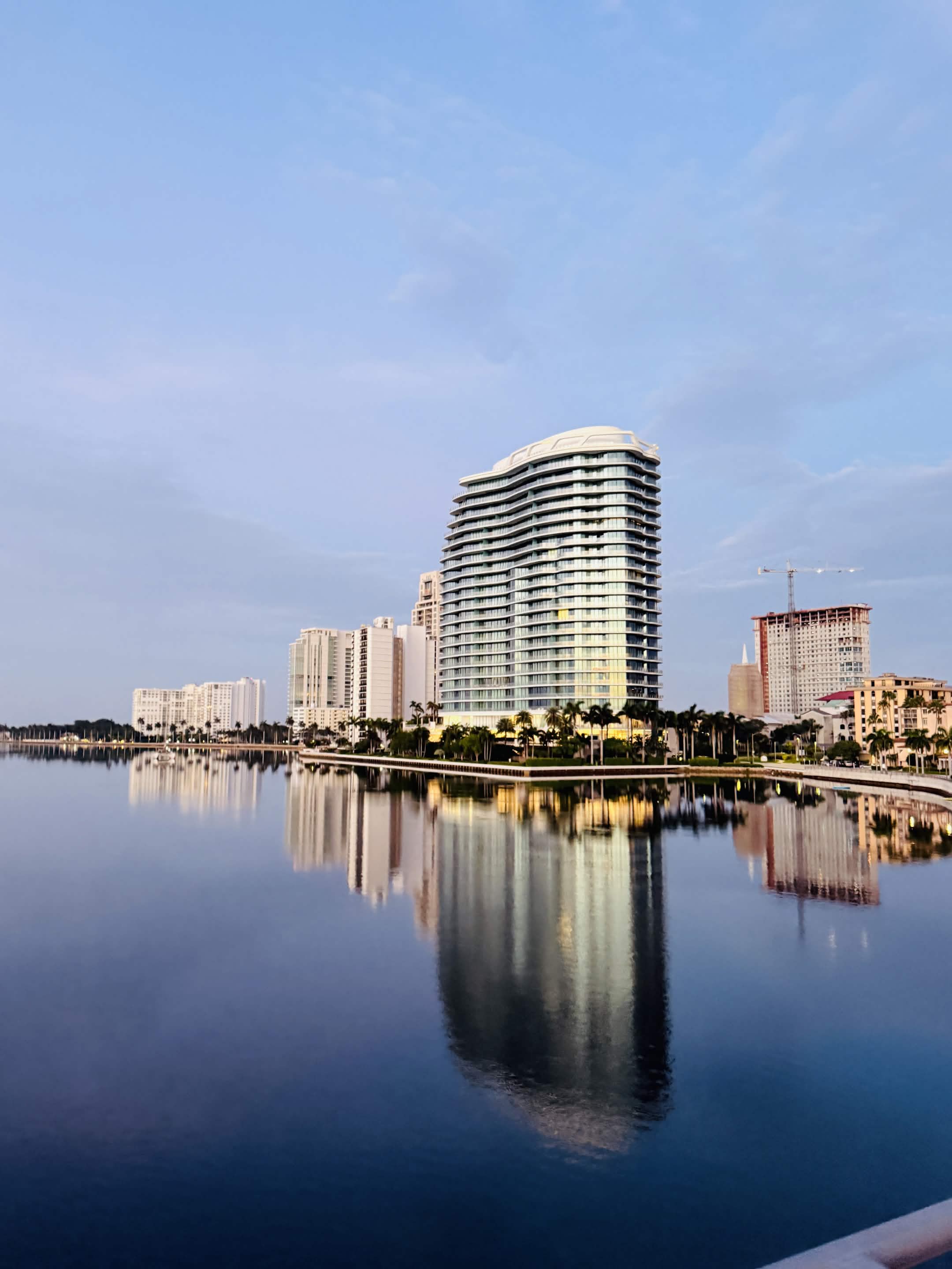 West Palm Beach waterfront at dawn — buildings reflected in still water.
